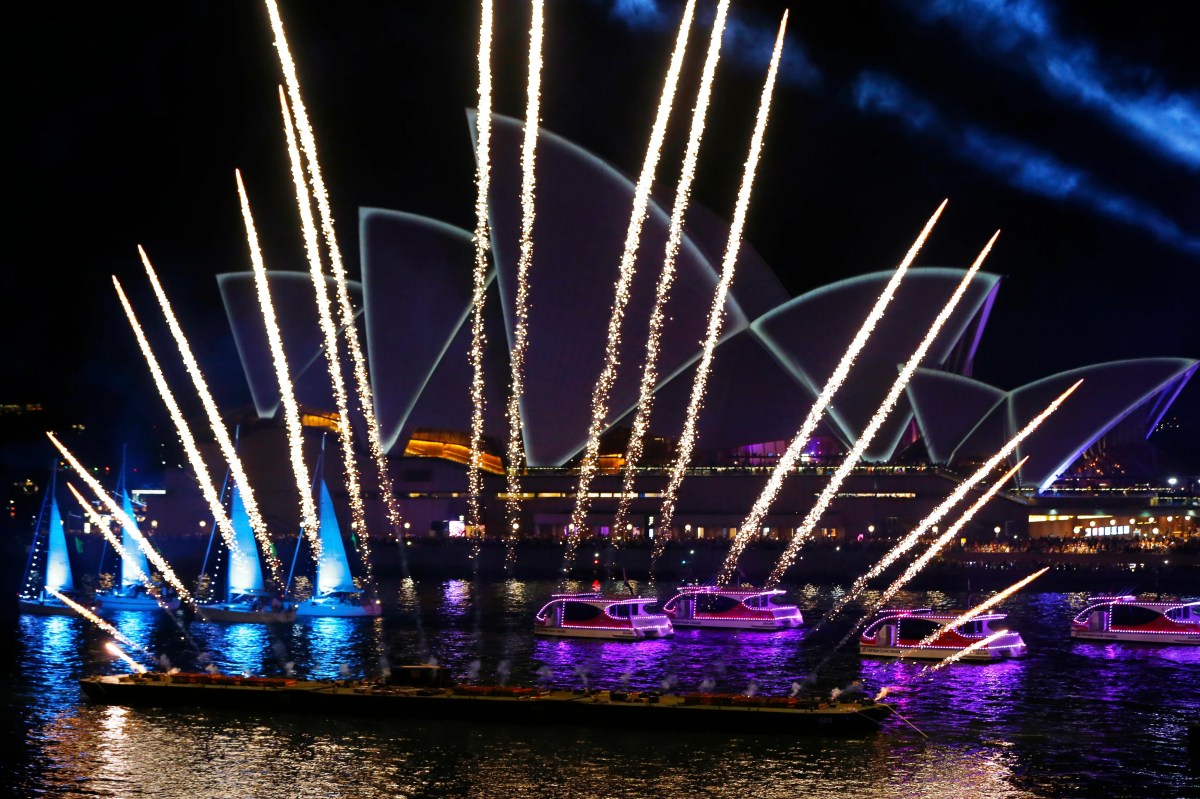Fireworks and boats with colorful lights near an iconic building at night.