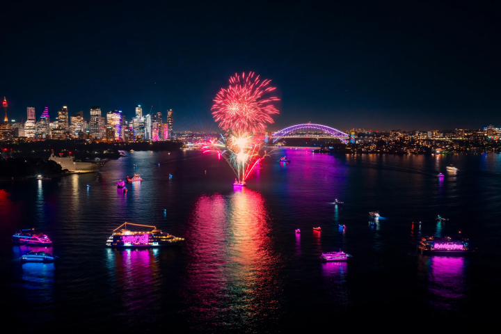 Fireworks over a city skyline with illuminated boats on water at night during VIVID Sydney on a cruise.