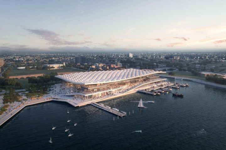 Aerial view of a modern waterfront building with a wavy roof and boats docked nearby.