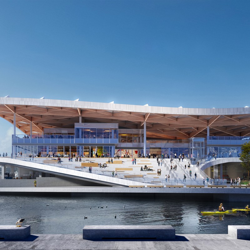 Modern waterfront building with sloped design and large canopy roof, people and kayaker in foreground.