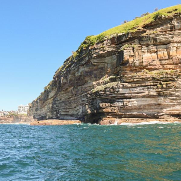 Rocky cliffside by the sea with blue water and clear sky.