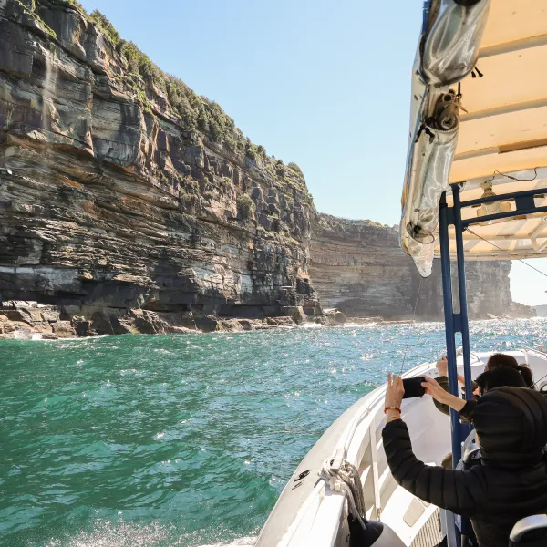 Boat with passengers viewing large rocky cliffs on a Sydney offshoire cruise.