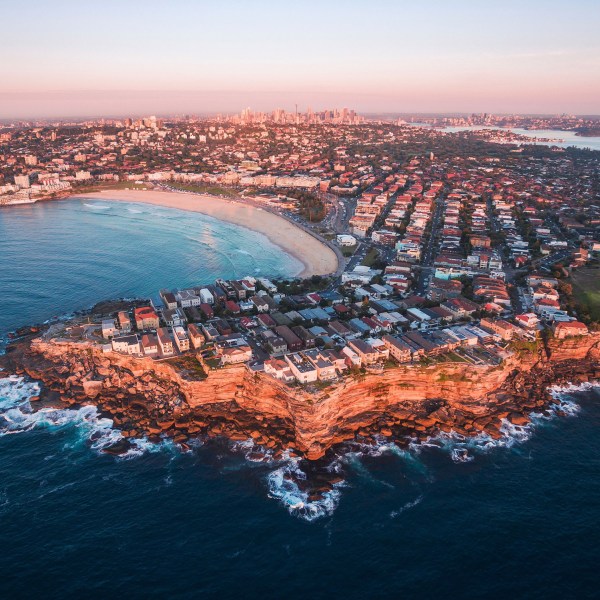 Aerial view of coastal city with beach, cliffs, and ocean at sunset.