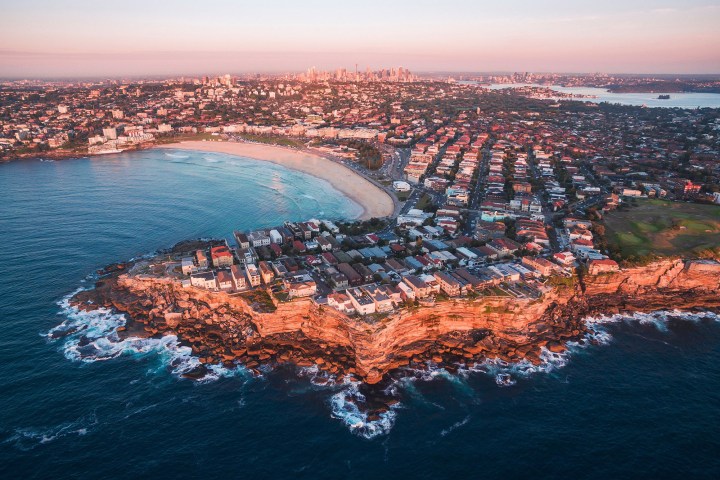 Aerial view of coastal city with beach, cliffs, and ocean at sunset.