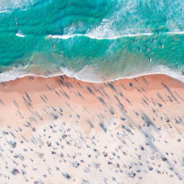 Aerial view of crowded beach with people and waves in turquoise sea.