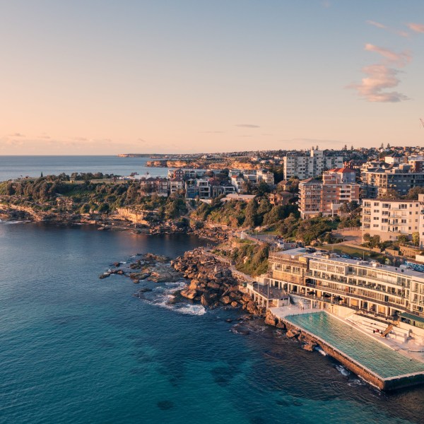 Coastal cityscape at sunset with buildings, rocky shore, and ocean pool.