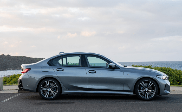 Side view of a gray car parked on a coastal road with ocean in the background.
