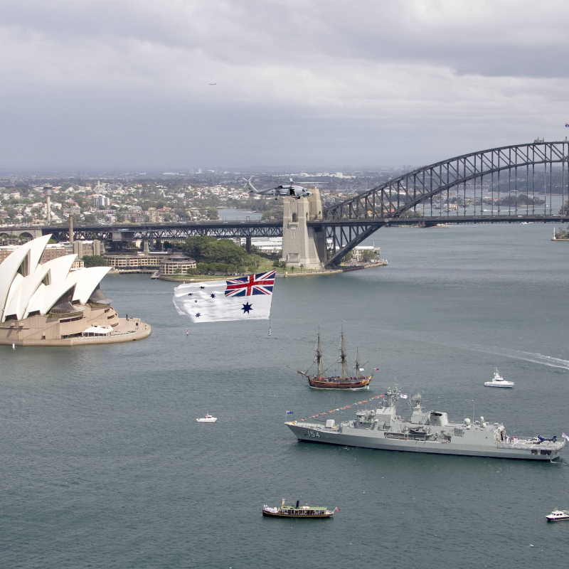 Sydney Opera House and Harbour Bridge with ships and flag over water.