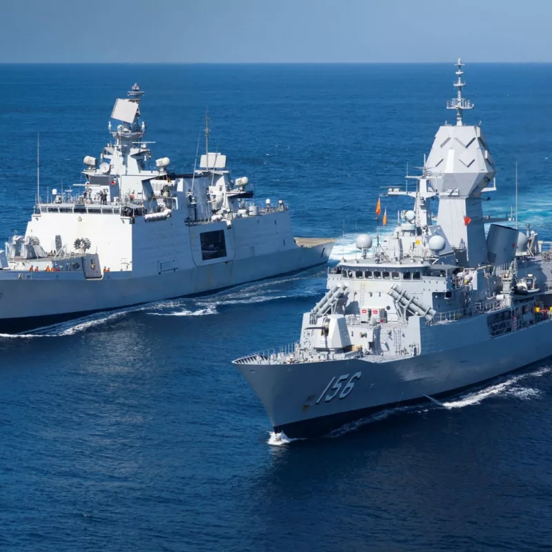 Two naval warships sailing side by side on a clear blue ocean.