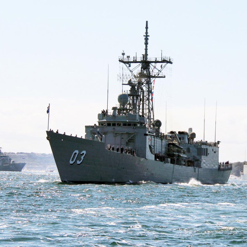 Three naval ships sail in formation on a sunny day with clear skies.