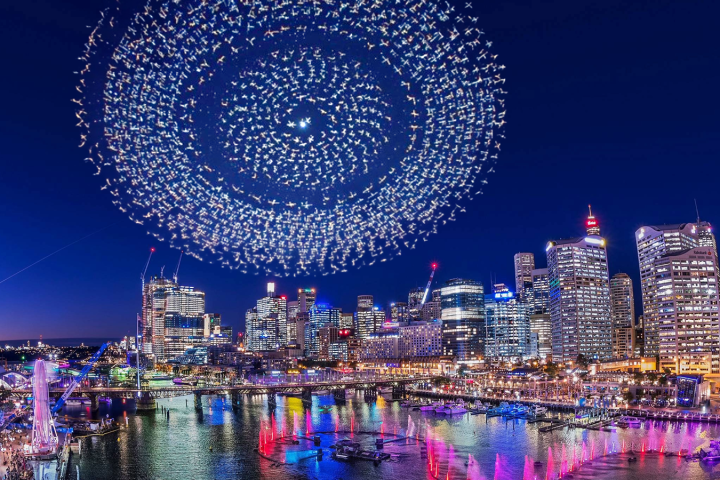 Cityscape at night with a large circular drone light display in the sky.