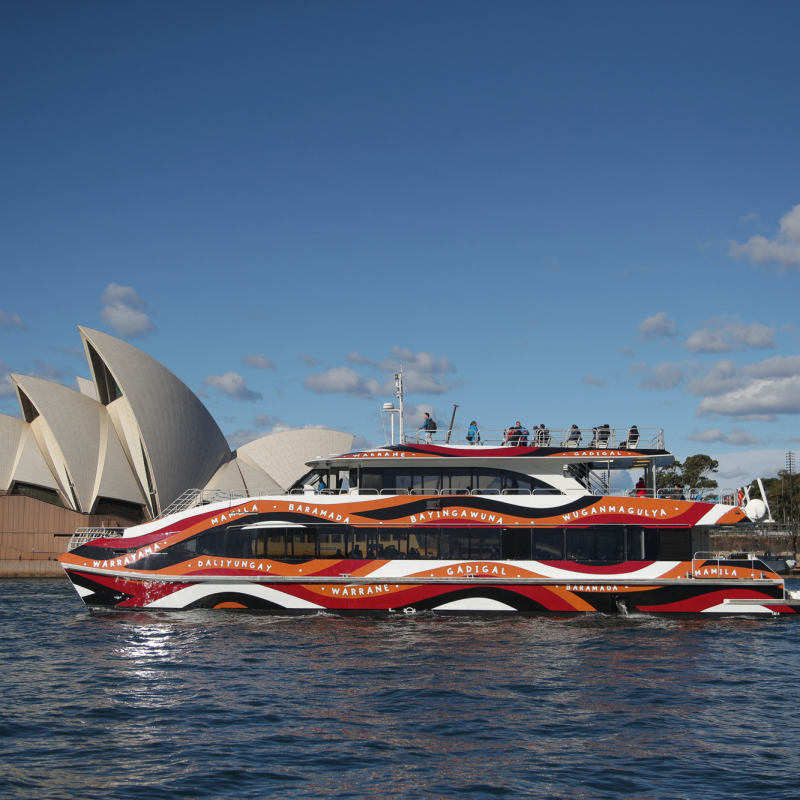 Colorful ferry near Sydney Opera House under a blue sky with clouds.