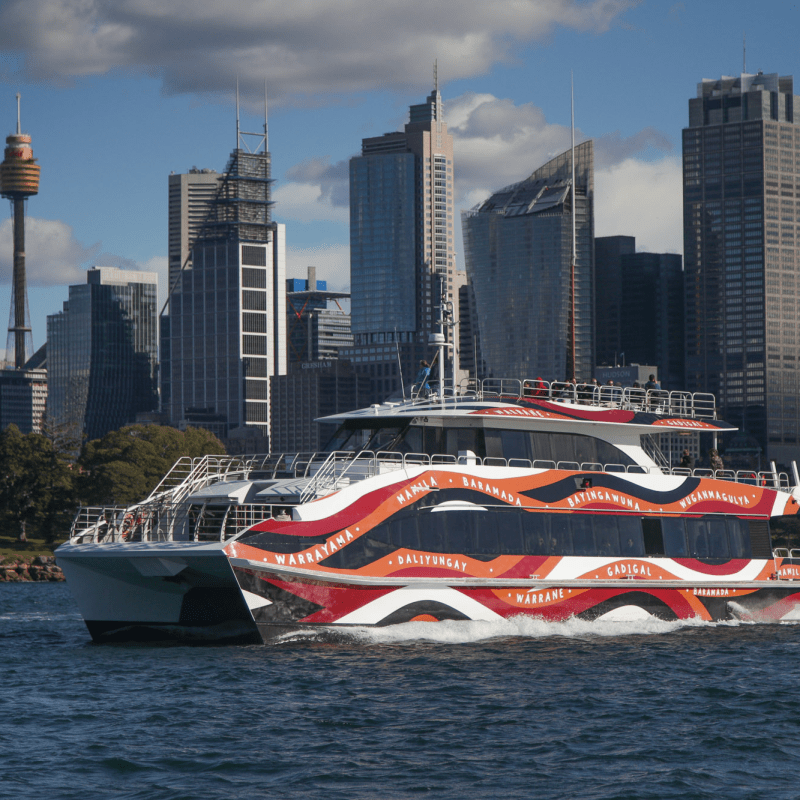 Colorful ferry on water with a city skyline in the background and partly cloudy sky.