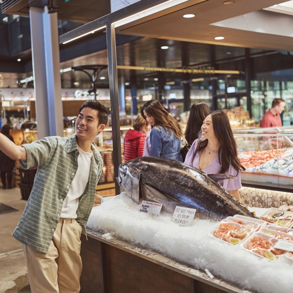 People taking a selfie with a large fish at a market stall.