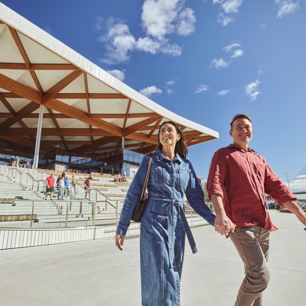 Smiling couple holding hands walking outside modern building on sunny day.