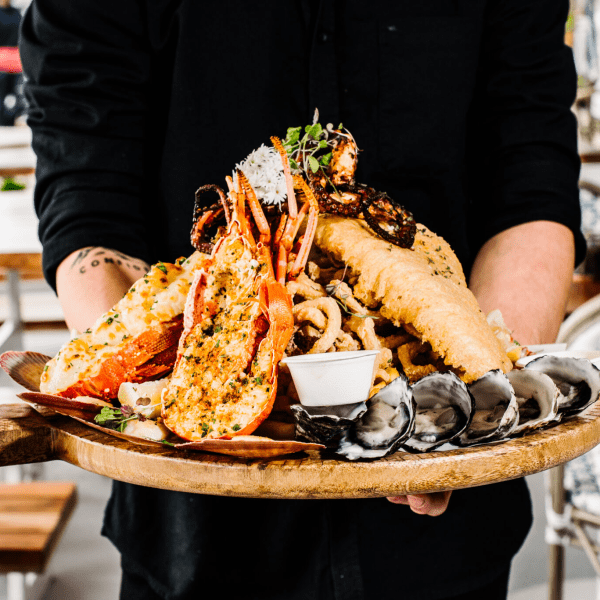 Person holding a platter with seafood assortment and dipping sauce.
