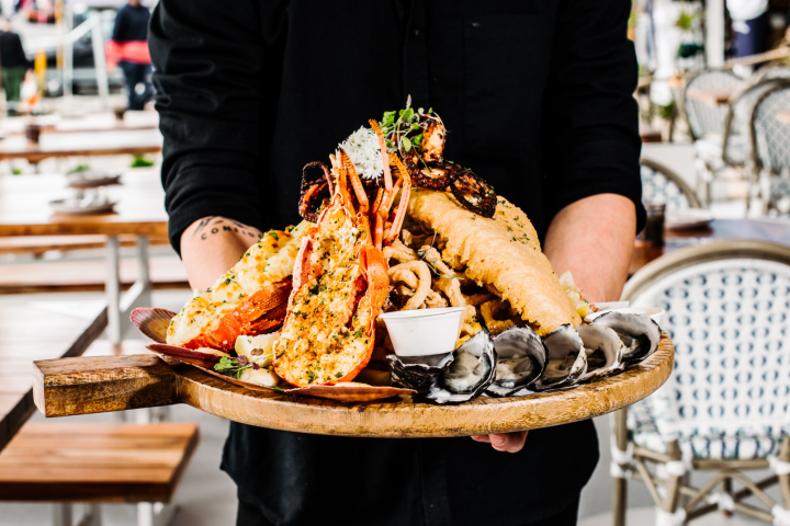 Person holding a platter with seafood assortment and dipping sauce.