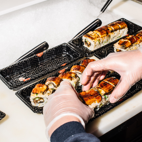 Person arranging sushi rolls in black trays on a counter.