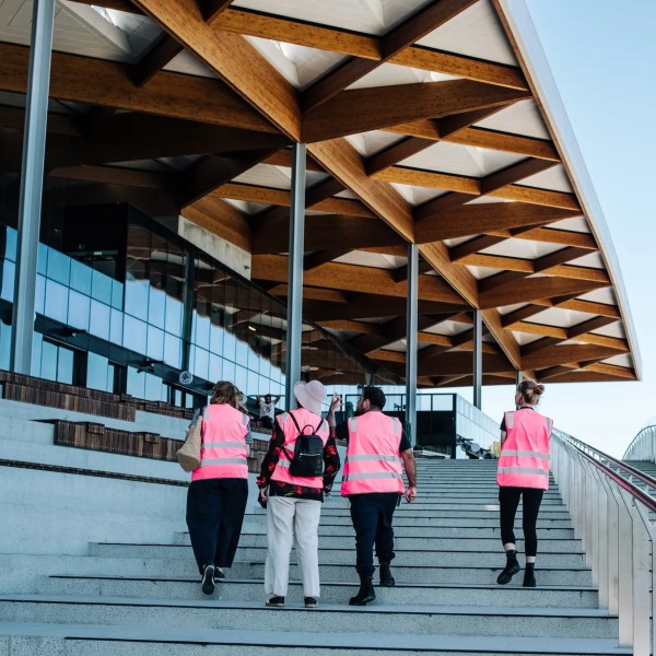 Four people in pink vests walking up large outdoor stairs next to a modern glass building.